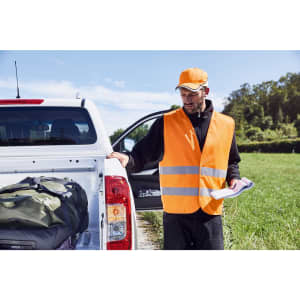 An orange safety vest with reflective stripes worn by a man near a vehicle, surrounded by greenery.