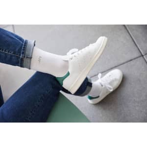 Function Sport Socks in white feature a logo, paired with white sneakers and denim jeans.