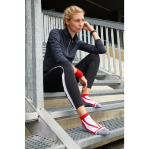A pair of red and grey sneaker socks worn by a woman sitting on metal stairs, dressed in athletic wear.