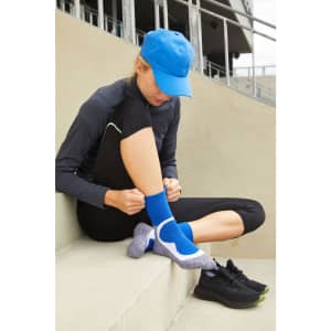 A person in a blue cap and black athletic wear adjusts their blue sports socks while seated on concrete steps.
