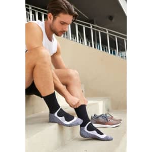 Black sport socks with a grey and white design, worn by a man sitting on steps beside running shoes.