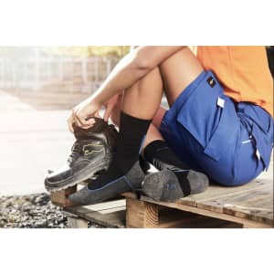 Worker socks in black and grey worn with work boots, paired with shorts, on a wooden pallet outdoors.