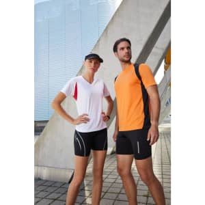 A model wears a vibrant orange men's running T-shirt paired with black shorts. The setting features modern architecture.