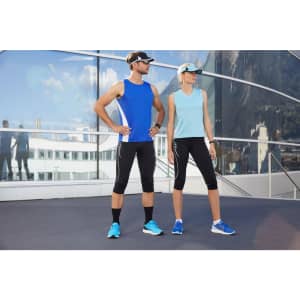 A man in a blue tank top and a woman in a light blue tank top, both wearing athletic gear, pose outdoors.