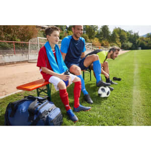 Team Socks in red and blue worn by players seated on a bench, with a soccer ball and gear on the grass field.