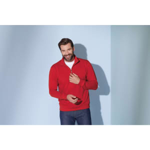A red Round-Neck Zip jumper with a zippered collar, worn by a smiling man against a blue background.