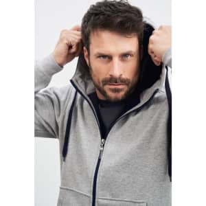 A man in a grey doubleface jacket with a navy hood, adjusting the hood in a neutral background.