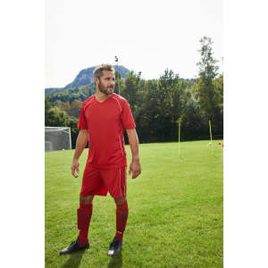 A red team shirt paired with matching shorts, displayed on a male model in an outdoor sports setting.