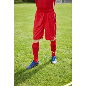 Red sports shorts with an elastic waistband, paired with blue shoes and red socks, situated on grass.