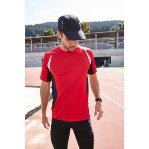A man wearing a red and black running t-shirt with a cap, standing on a sports track.