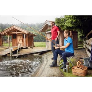 A red and a blue men's polo shirt on two people fishing by a pond, with wooden huts in the background.