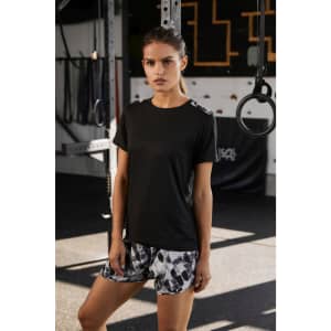 A ladies' black sports shirt displayed with patterned shorts, set against a gym backdrop with equipment.