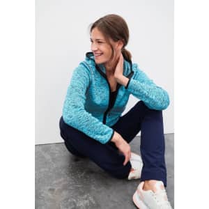 A blue knitted fleece hoodie with a zip and hood, paired with navy pants, worn by a smiling woman sitting on the floor.