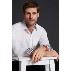 A plain white button-up shirt with checkered cuffs, worn by a man seated on a white stool. The background is dark.