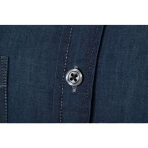 A close-up of a blue denim shirt featuring a button and stitching detail. The fabric has a textured appearance.