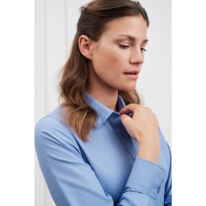 A light blue button-up shirt with a collar, featuring a model showcasing the garment. The shirt has long sleeves and a logo.
