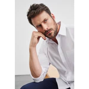 A model in a white long-sleeve button-up shirt, posing thoughtfully with one hand on his chin.