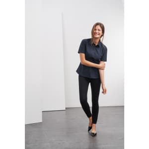 A model is wearing a navy blue button-up shirt paired with black fitted pants and high heels. The shirt features a collar and a subtle design.