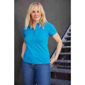 A blue ladies' polo shirt displayed on a woman standing near a staircase. The shirt features a collar and a logo.