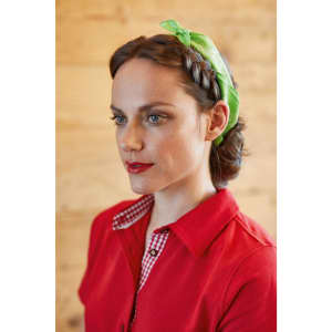 A red polo shirt is worn by a woman with a green headband, featuring a checkered collar. The background is wooden.