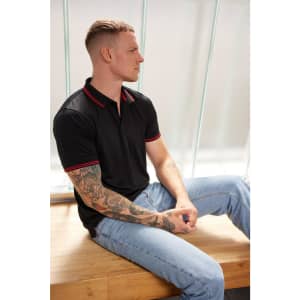 A black polo shirt with red accents is worn by a man sitting on a wooden bench, showcasing its functional design.