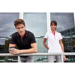A black and a white polo shirt with red detailing, showcased by a male and a female model. Both models are standing outdoors.