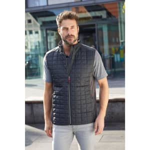 A man wears a charcoal knitted hybrid vest, featuring a quilted design and a zipper, set against a modern urban backdrop.