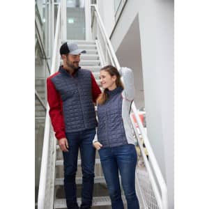 A grey and red knitted hybrid jacket is worn by a man and a woman, standing on a staircase. Both wear casual jeans.