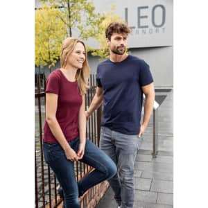A maroon women's t-shirt and a navy men's t-shirt are worn by a model couple outdoors. Both shirts feature a logo.