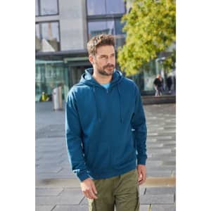 A man wearing a blue zip hoodie stands outdoors, surrounded by modern architecture and greenery.
