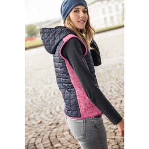 A knitted hybrid vest in navy blue and pink, featuring a hood and a fitted design. The model is wearing it outdoors.