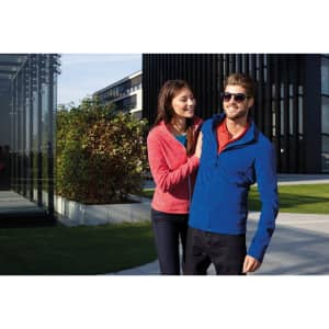 A red ladies fleece jacket and a blue men's fleece jacket are worn by a couple outdoors. Both jackets have a logo.