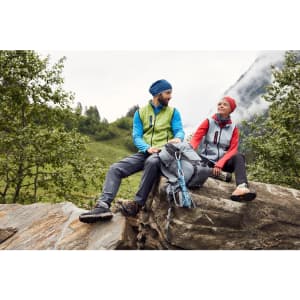 A green and blue knitted fleece vest is worn by a man, while a red vest adorns a woman. Both are outdoors in nature.