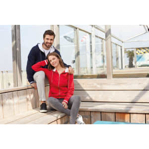 A red track jacket is worn by a seated woman, while a man beside her wears a navy jacket. Both are in a bright setting.