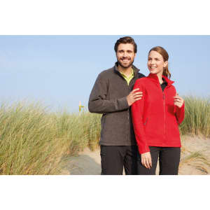 A polar fleece jacket in red, worn by a woman, alongside a man in a grey fleece jacket, with a natural background.
