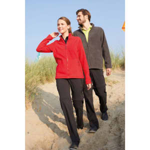 A red fleece jacket worn by a woman, accompanied by a man in a grey fleece jacket, walking on sandy terrain.