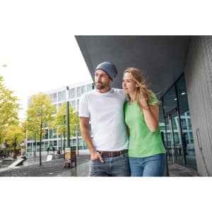 A man in a white shirt and a woman in a green t-shirt stand together outdoors near modern buildings.