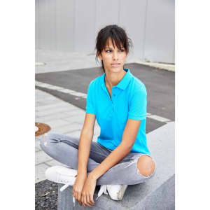 A woman wearing a bright blue polo shirt and grey ripped jeans, sitting on a stone bench outdoors.