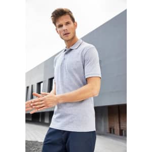 A grey polo shirt featuring a collar and short sleeves, displayed by a man outdoors. The shirt has a logo.
