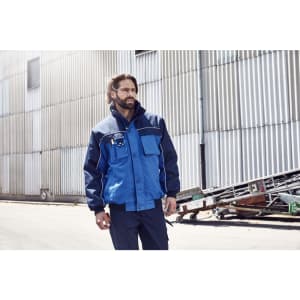 A workwear jacket in navy and blue, featuring a front pocket and logo, worn by a man in an industrial setting.