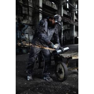 A workwear jacket in dark grey is worn by a person using a grinder, creating sparks in an industrial setting.
