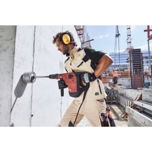 A workwear vest in light beige with dark green accents, worn by a person using a power drill on a construction site.