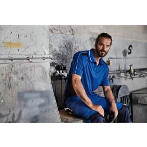 A blue polo shirt worn by a man sitting in a workshop, with tools and equipment in the background.