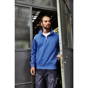 A blue half zip sweat jumper with a collar, worn by a man standing at a doorway, featuring a logo on the chest.