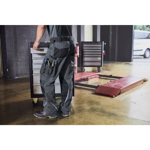 Workwear pants in black, featuring pockets, being worn by a person moving a tool trolley in an industrial setting.