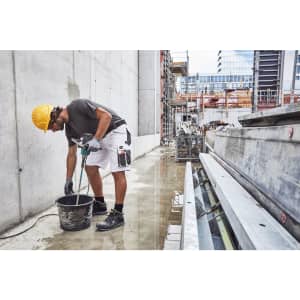 Workwear Bermudas in white, worn by a worker mixing material at a construction site, with a hard hat and tools.