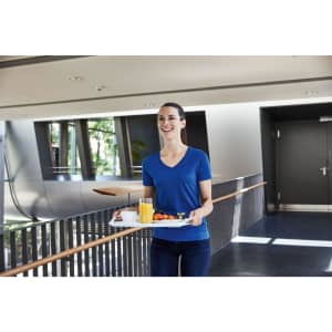 A woman in a blue V-neck t-shirt carries a tray with food and beverages in a modern interior space.