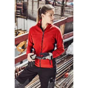 A red polar fleece jacket with a zip, worn by a woman, featuring a logo, set in a construction environment.
