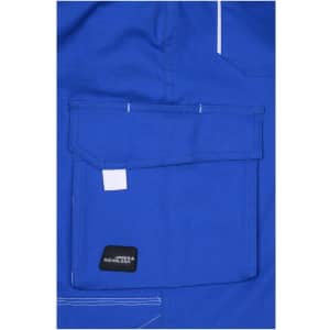 A close-up of blue workwear pants featuring a large front pocket and a branding label.