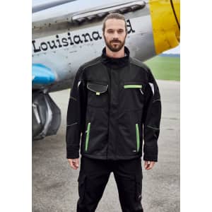 A man wearing a black workwear softshell jacket with green accents, standing in front of an aircraft. The jacket features a logo.